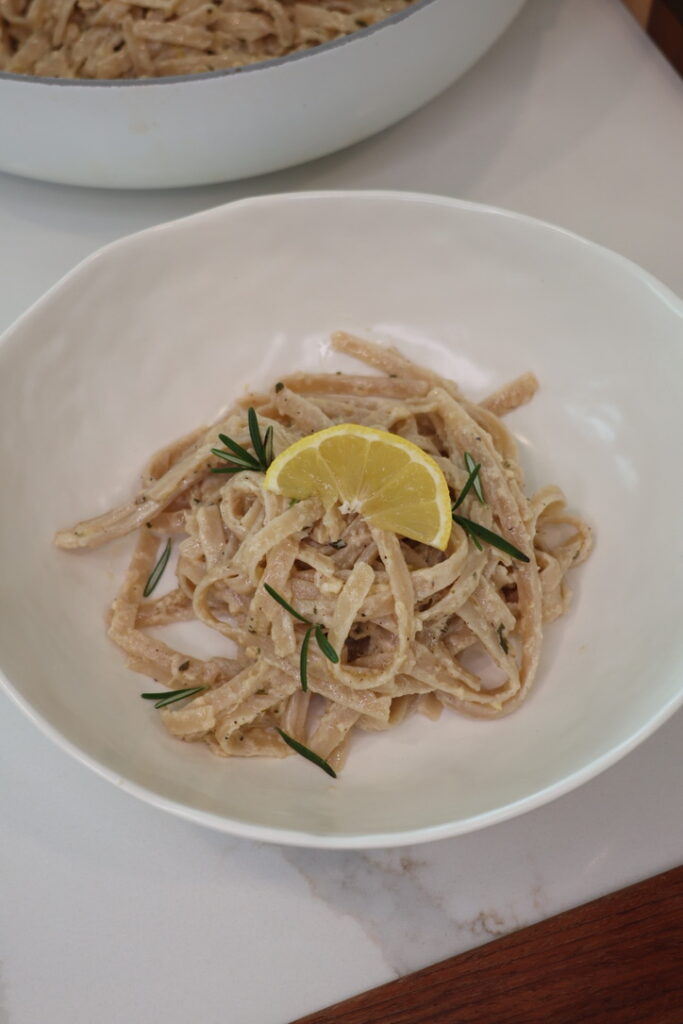 A bowl of creamy lemon fettuccine Alfredo made with gluten-free brown rice fettuccine noodles tossed in a rich sauce of blended cottage cheese, heavy cream, freshly grated Parmesan, garlic, fresh rosemary, lemon juice, and lemon zest. Garnished with extra Parmesan, cracked black pepper, rosemary, and lemon zest for a fresh, high-protein pasta dinner.