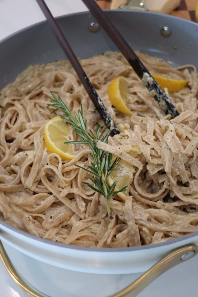 A bowl of creamy lemon fettuccine Alfredo made with gluten-free brown rice fettuccine noodles tossed in a rich sauce of blended cottage cheese, heavy cream, freshly grated Parmesan, garlic, fresh rosemary, lemon juice, and lemon zest. Garnished with extra Parmesan, cracked black pepper, rosemary, and lemon zest for a fresh, high-protein pasta dinner.