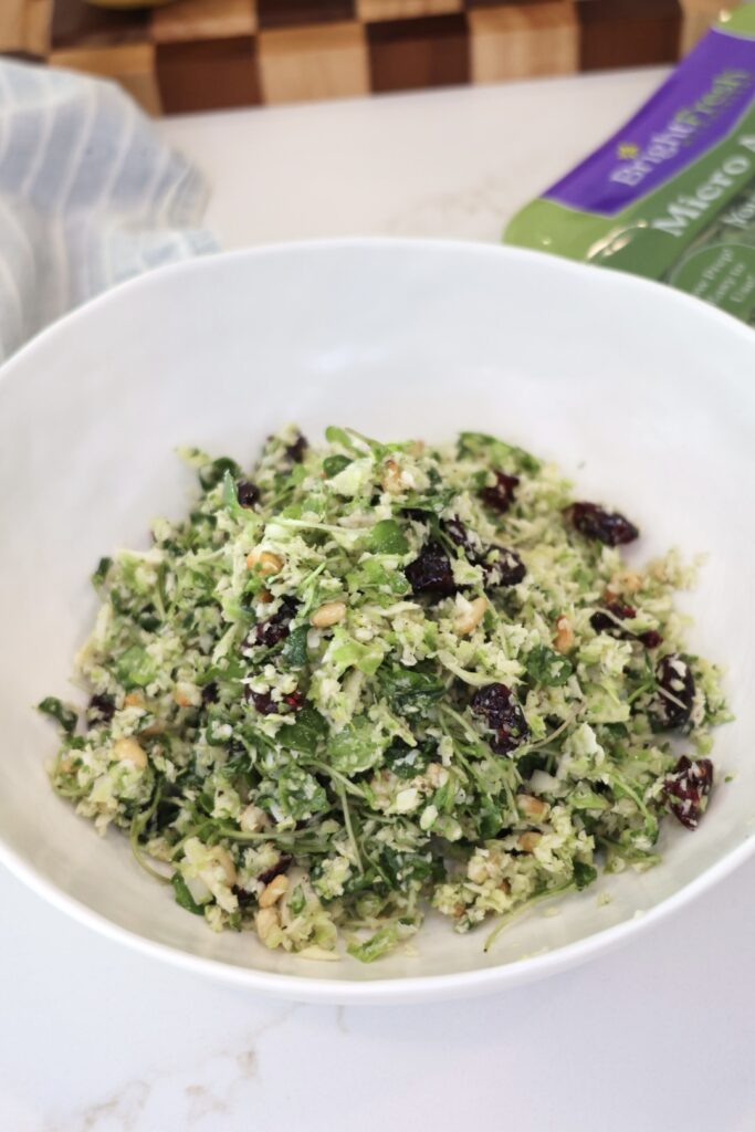 A bowl of lemony shaved Brussels sprouts salad with freshly grated Parmesan cheese, toasted pine nuts, dried cranberries, and arugula microgreens. This healthy Brussels sprouts salad is a fresh, crunchy side dish perfect for meal prep, BBQs, or weeknight dinners.
