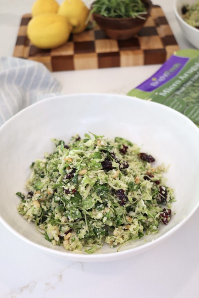 A bowl of lemony shaved Brussels sprouts salad with freshly grated Parmesan cheese, toasted pine nuts, dried cranberries, and arugula microgreens. This healthy Brussels sprouts salad is a fresh, crunchy side dish perfect for meal prep, BBQs, or weeknight dinners.